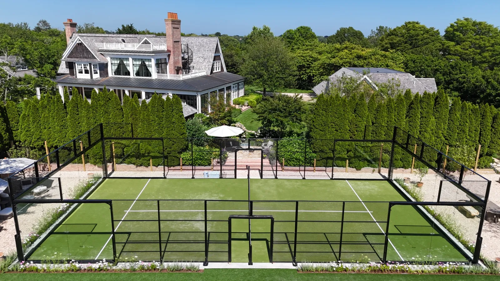 Residential padel court with green turf behind a shingle-style house in New England